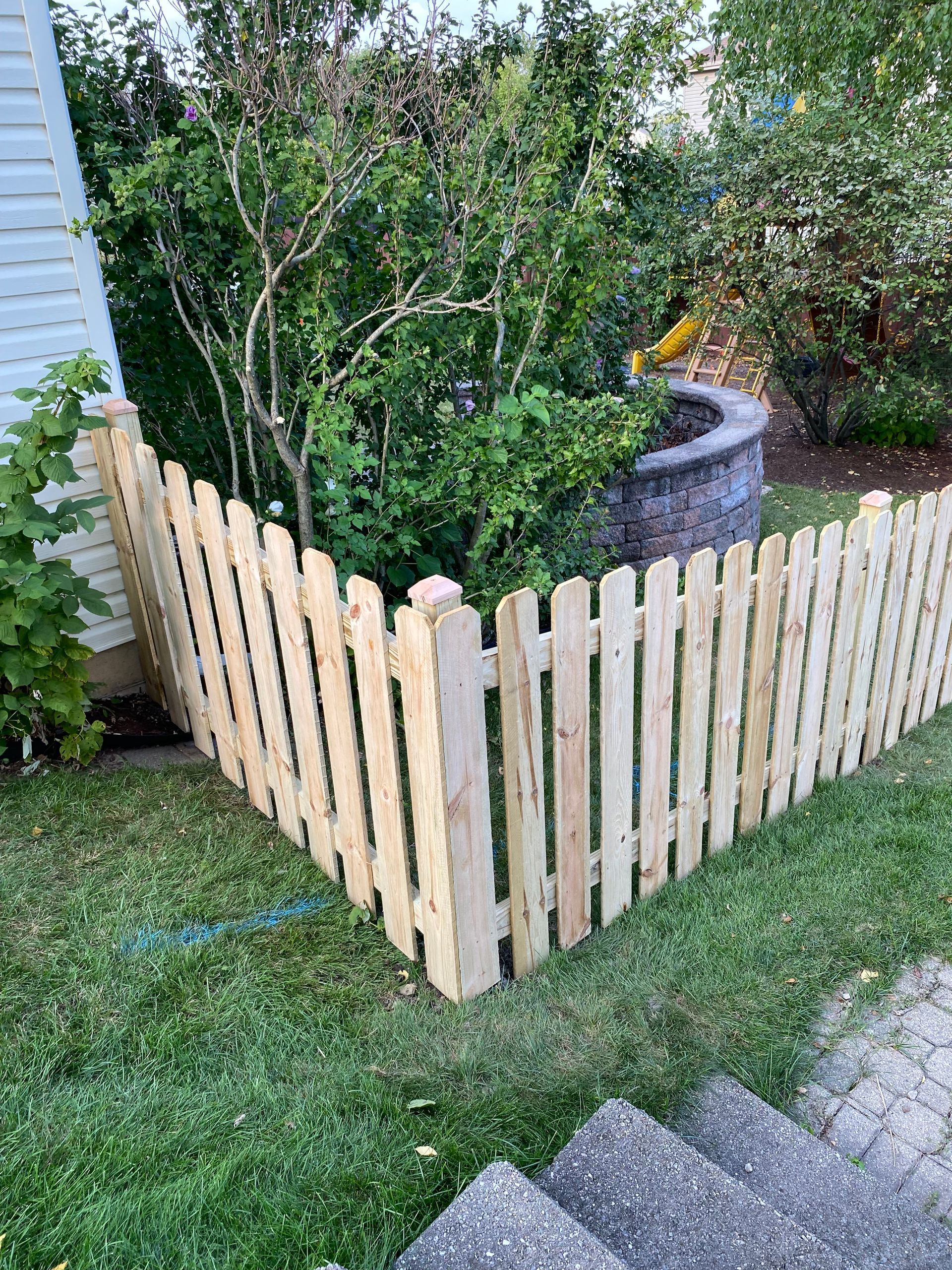 A wooden picket fence is sitting on top of a lush green lawn.