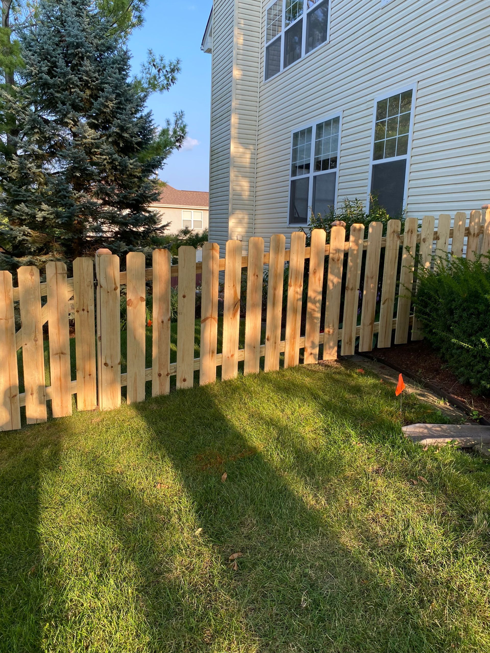 A wooden picket fence is in the backyard of a house.