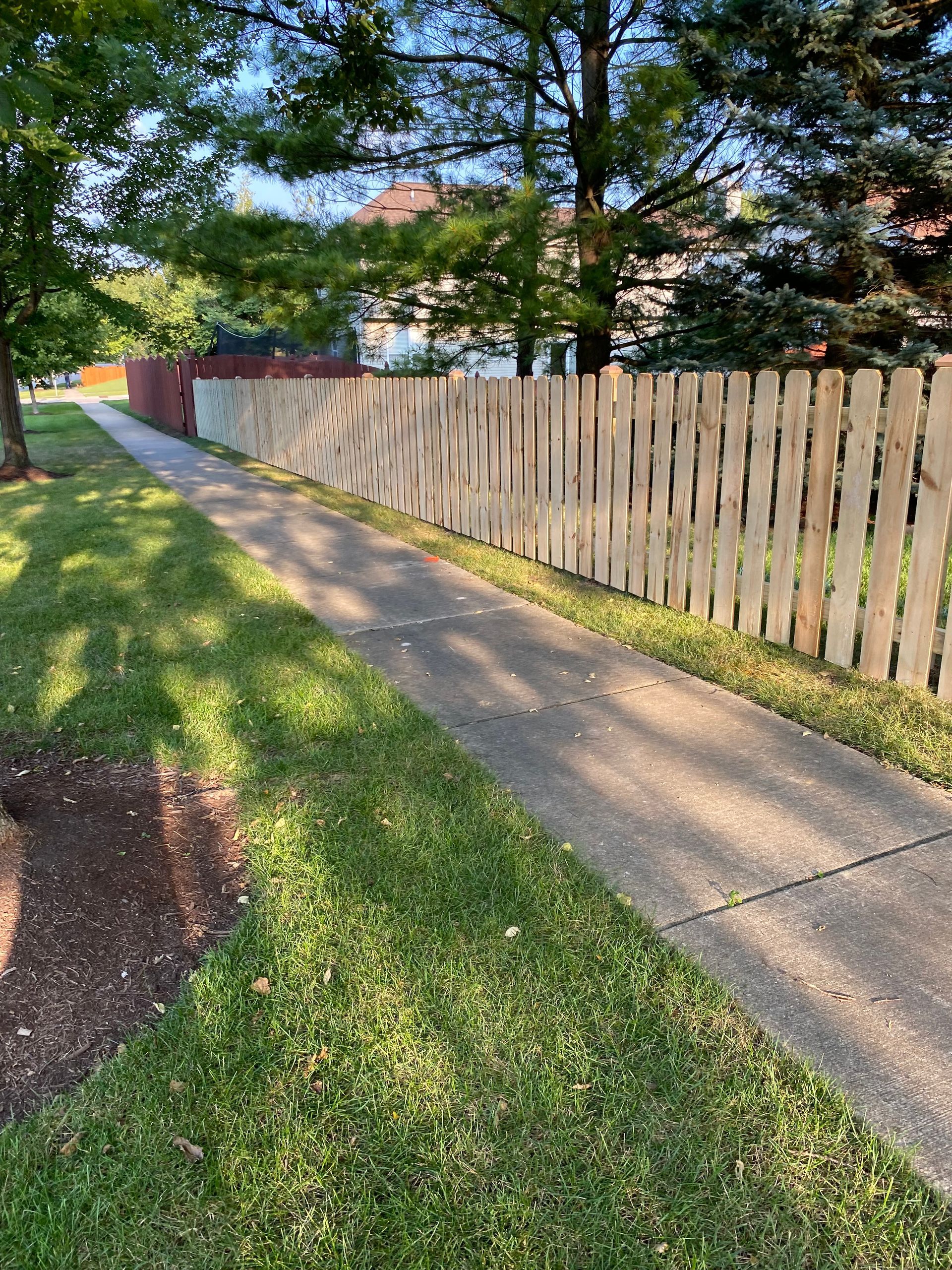 A wooden fence along a sidewalk next to a lush green lawn.
