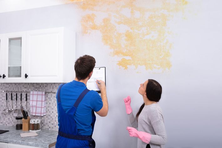 A man and a woman are looking at a damaged wall in a kitchen.