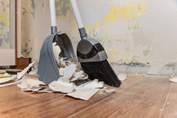A broom and a shovel are sitting on a wooden floor.