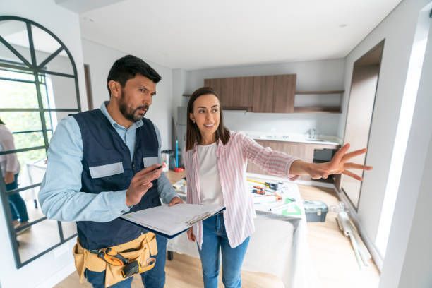 A man and a woman are standing in a kitchen looking at a window.