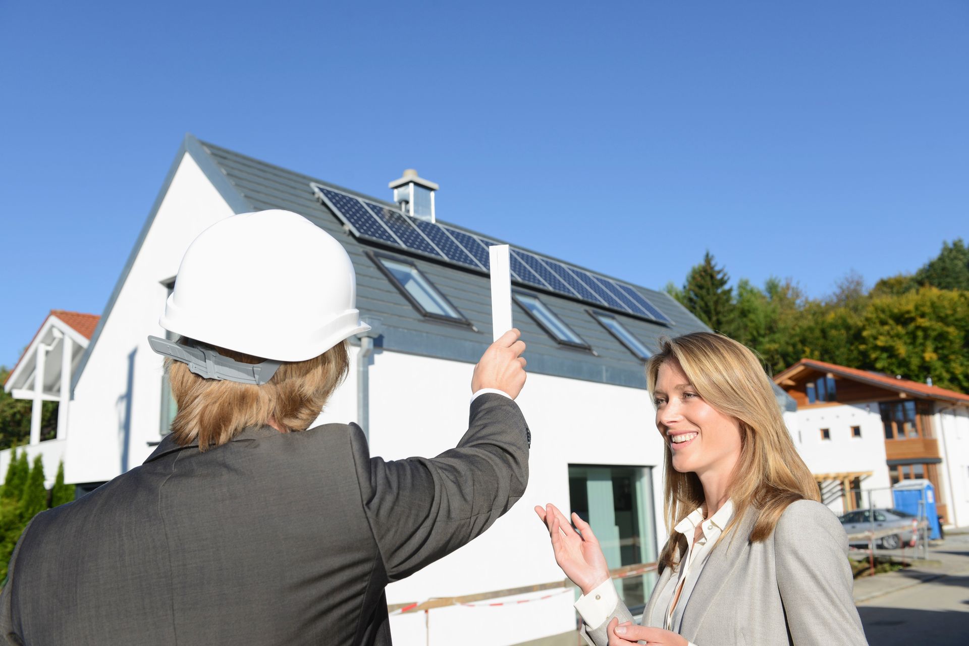 A man and a woman are standing in front of a house with solar panels on the roof.