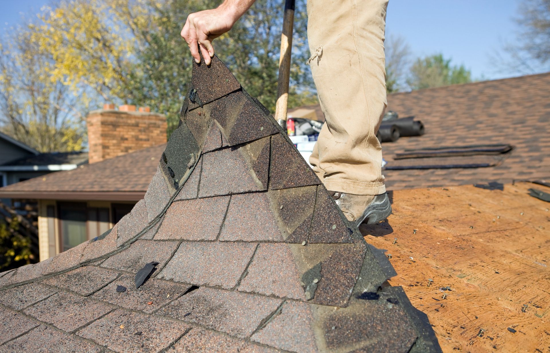 A man is standing on top of a roof holding a pile of shingles.