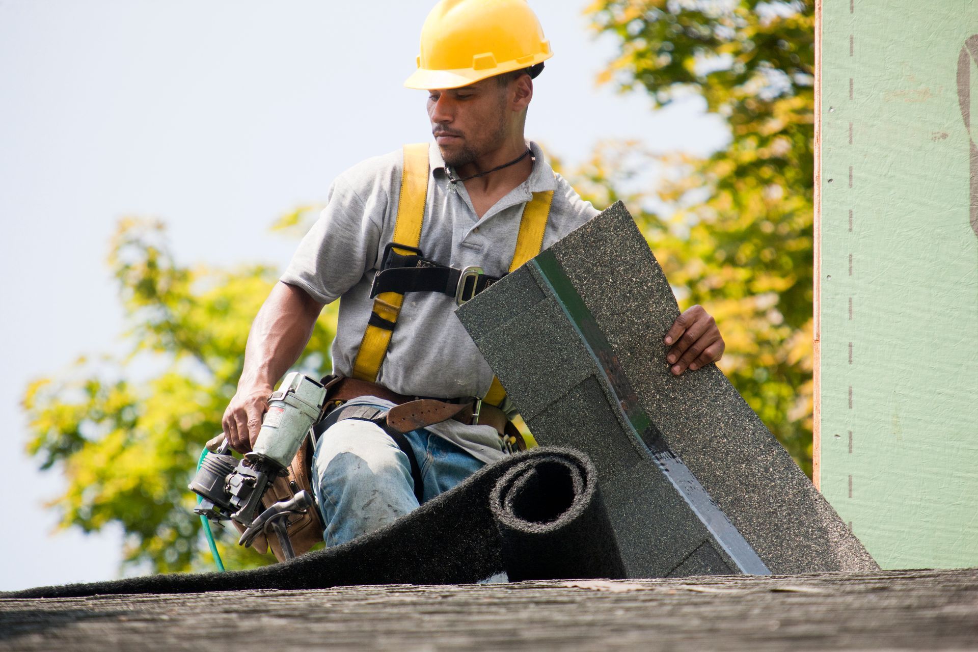 A man wearing a hard hat is working on a roof.