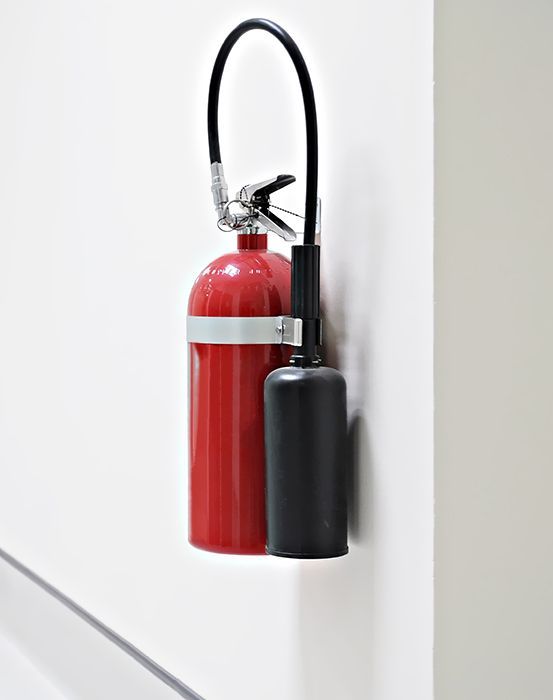 Un extintor rojo está colgado en una pared blanca.