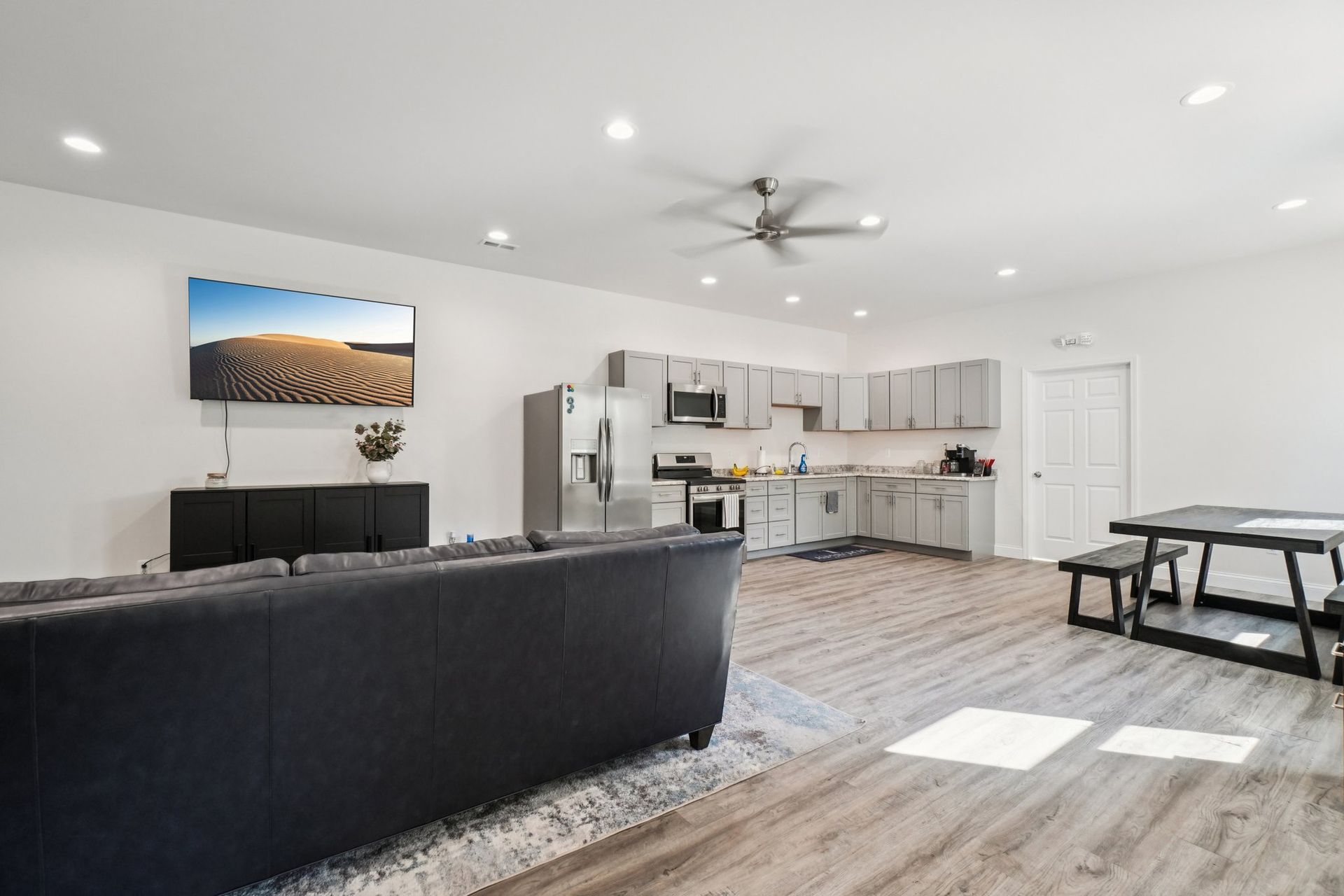 Spacious modern living space with kitchen, sofa, TV, and dining area. Light gray walls, wood-look floors.
