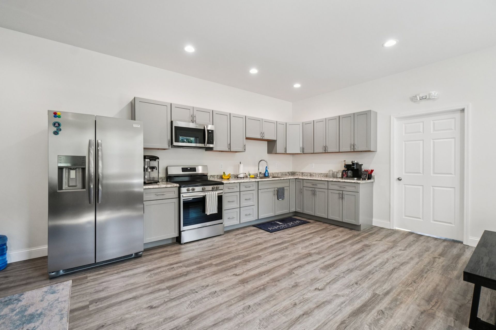 Modern kitchen with stainless steel appliances, gray cabinets, and light wood-look flooring.