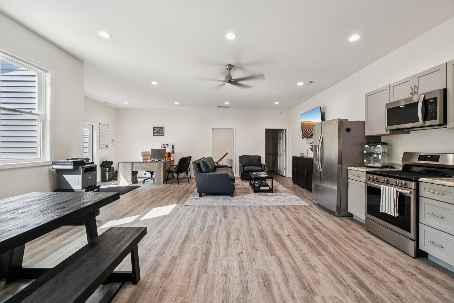 Spacious open-concept living space with kitchen, dining table, office area, and seating. Gray and neutral tones.