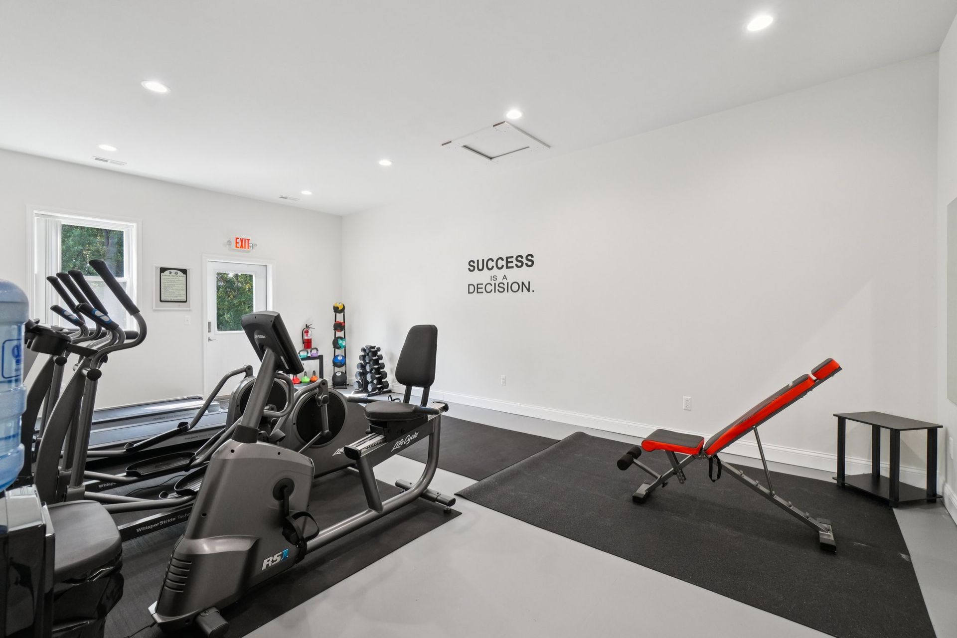 Home gym with cardio machines, weights, and adjustable bench on gray and black flooring.