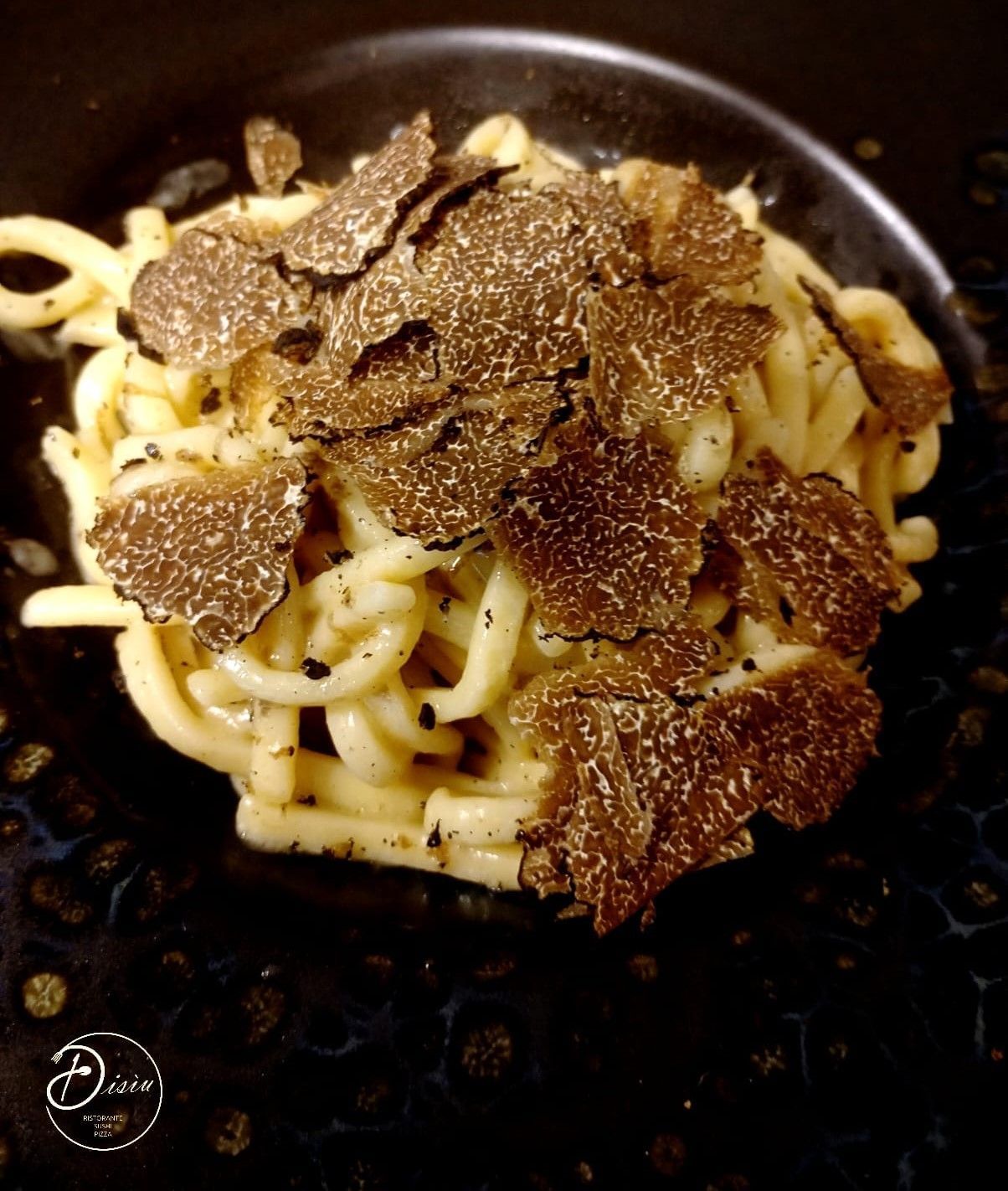 Piatto di pasta guarnito con fettine di tartufo su un piatto scuro.