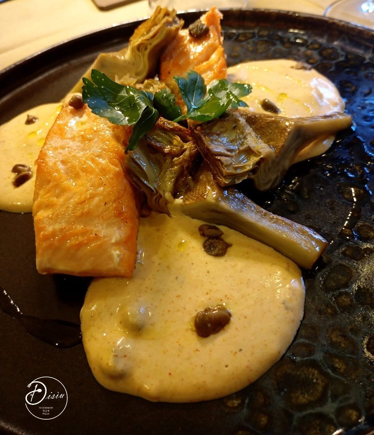Salmone con carciofi e salsa cremosa, guarnito con prezzemolo e capperi su un piatto scuro.