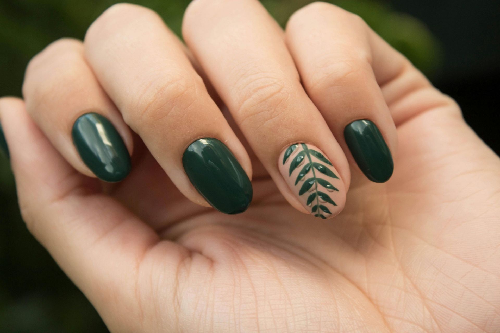 A close up of a woman 's hand with green nails and a leaf design.