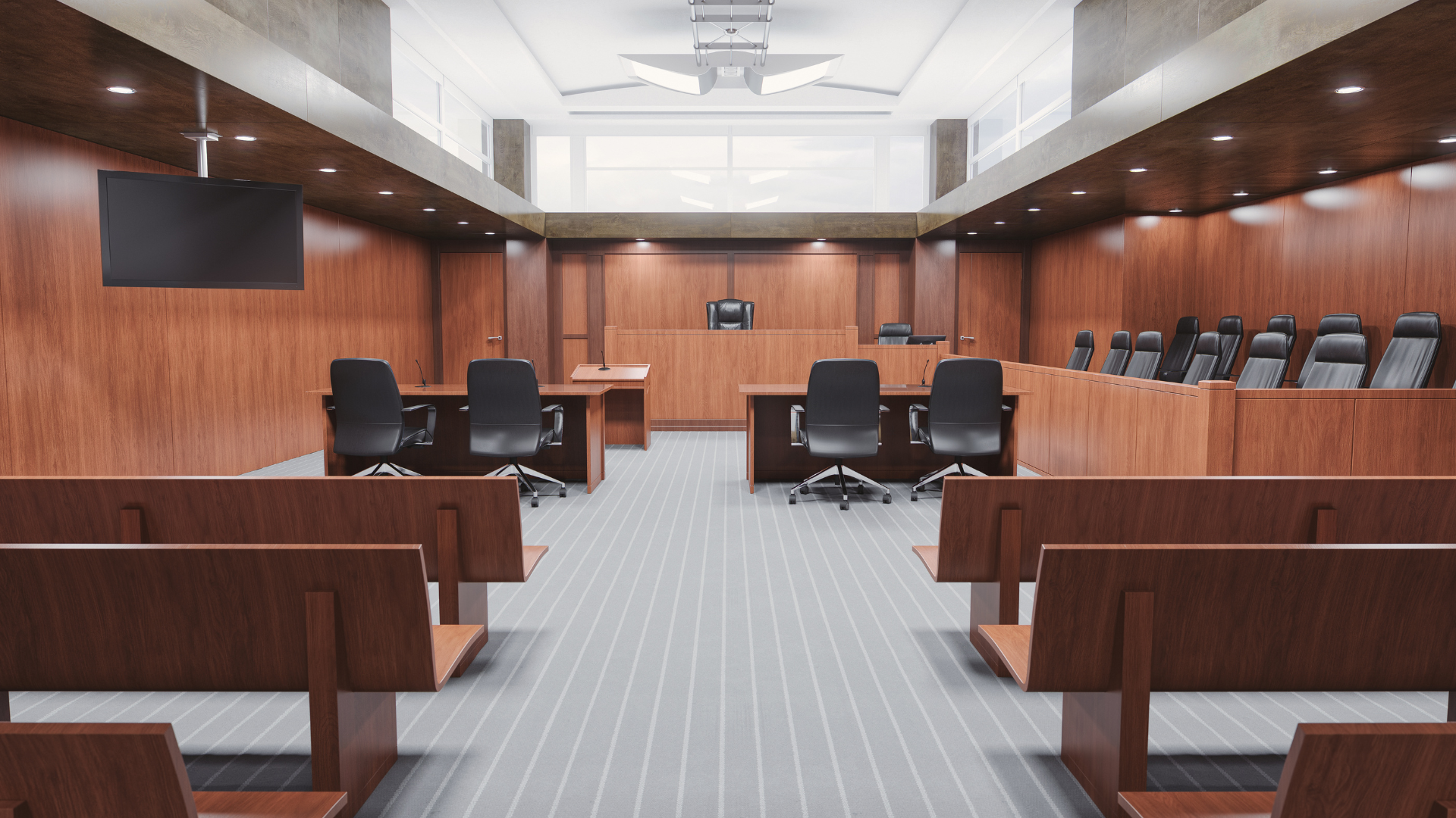 Empty courtroom with wooden paneling, benches, desks, and chairs.