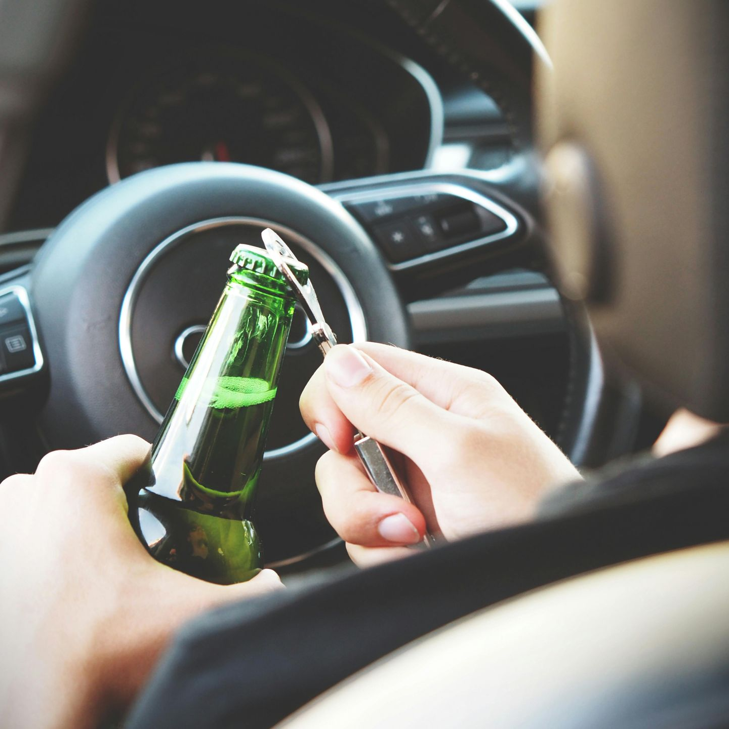 Person opening a beer bottle while sitting in the driver's seat of a car.