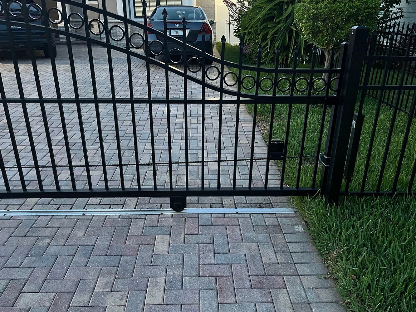 Ornate black gate leads to brick walkway and entry