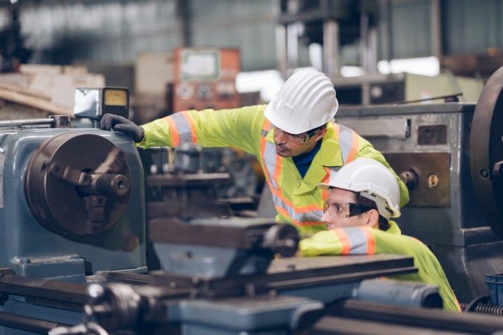 Two workers in hard hats collaborating on a metal piece