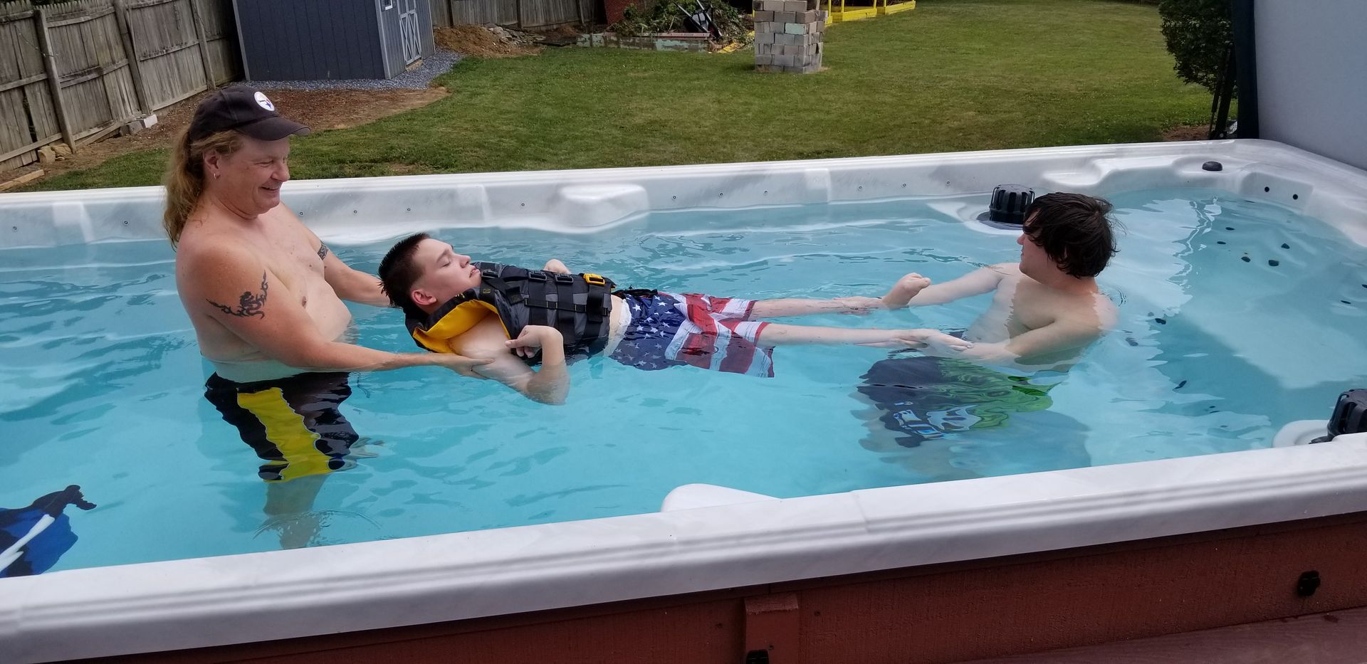 Woman and child in a pool, supporting another child wearing a life vest.