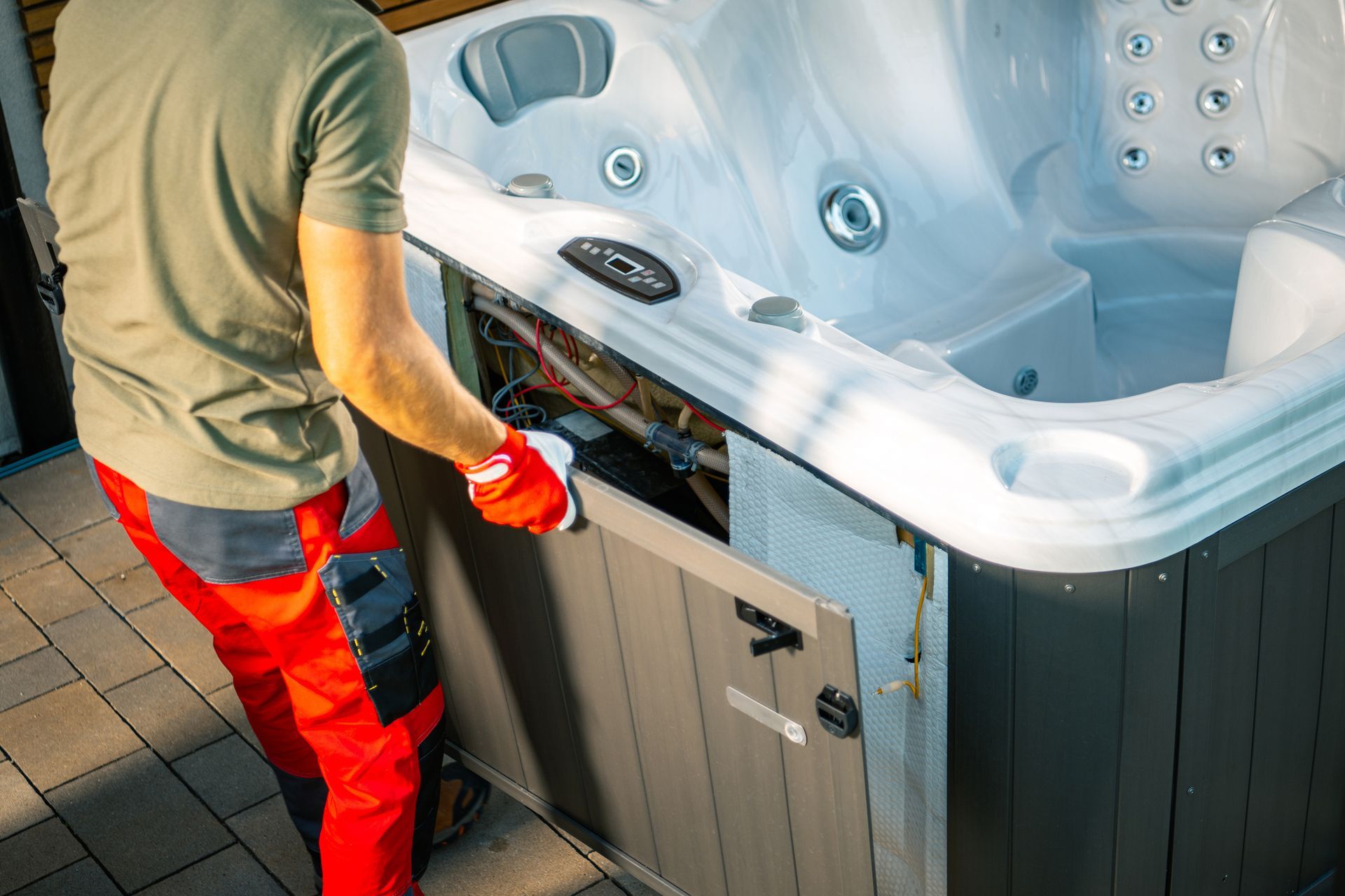 A male professional technician wearing red gloves works on hot tub repair.