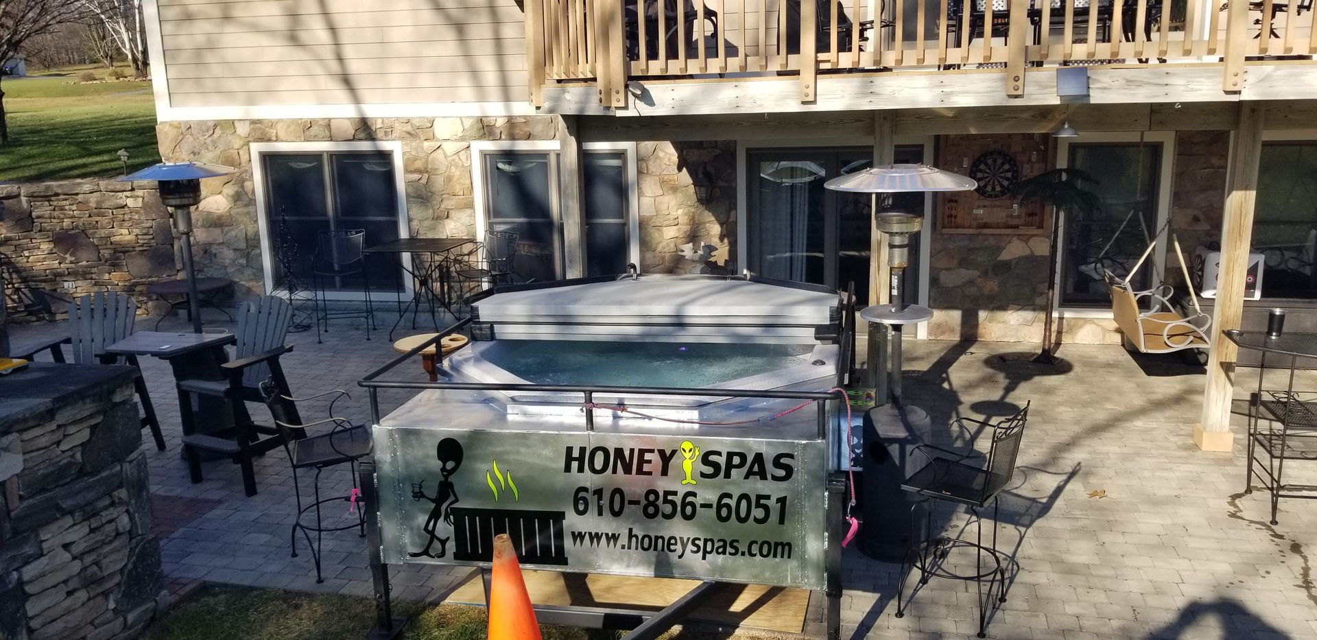 A hot tub on a patio in front of a house with Honey Spas sign.