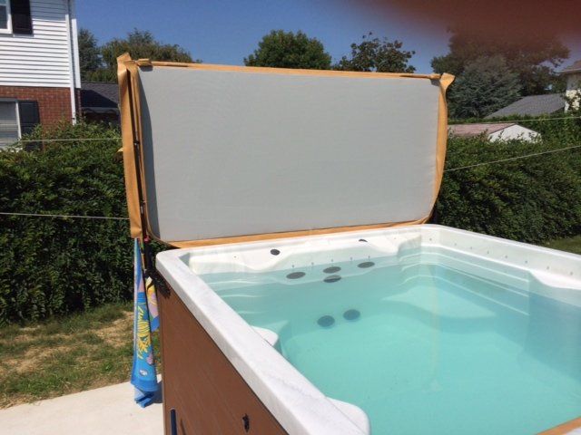 A hot tub with a partly open gray cover in a sunny backyard.