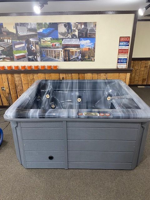 Gray hot tub on display, with a dark marble-look interior, in a showroom.
