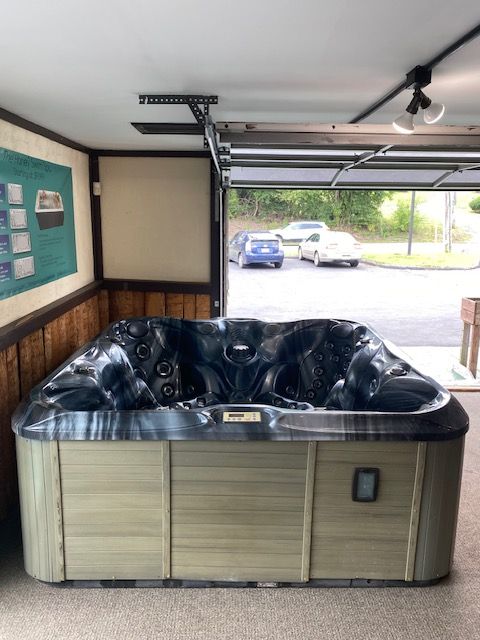 Hot tub displayed in a partially open garage.  The tub has a dark interior, light wood-colored exterior, and is indoors.