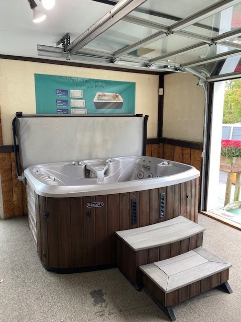 Hot tub display in showroom with steps. Dark wood siding and light gray trim.