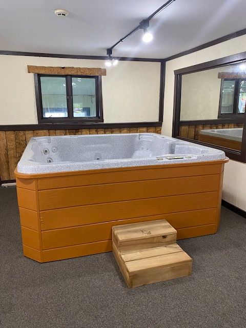 A rectangular orange hot tub with a wooden step in a room with a window and mirror.