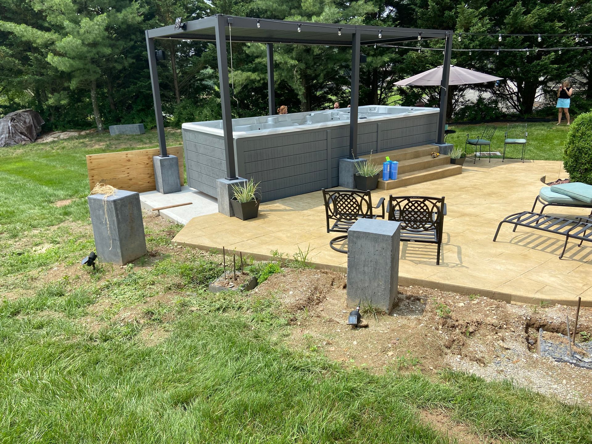 Backyard with hot tub under pergola, concrete patio, and green lawn.
