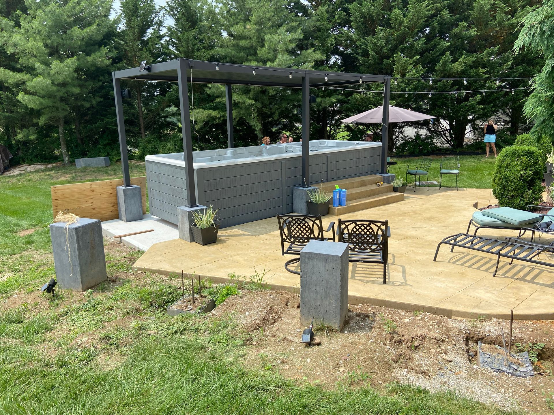 Backyard with a grey hot tub under a pergola, a concrete patio, and seating.