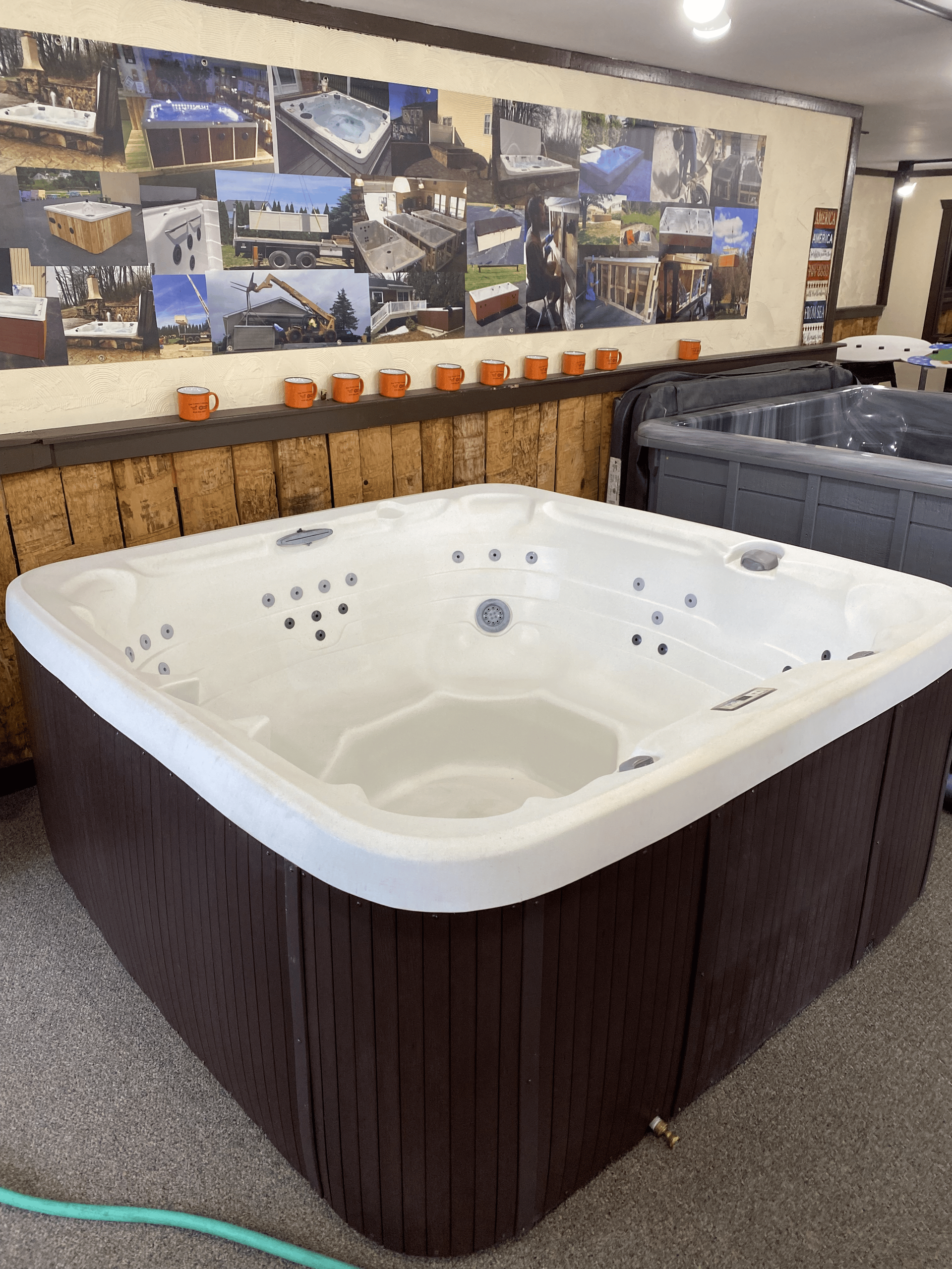 Square hot tub with brown skirting, white interior, in a showroom.