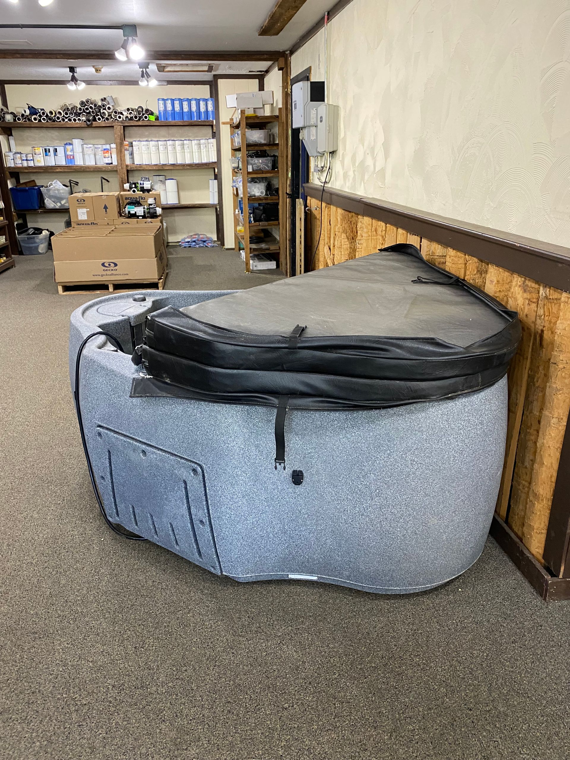 A small, gray hot tub with a black cover sits indoors.