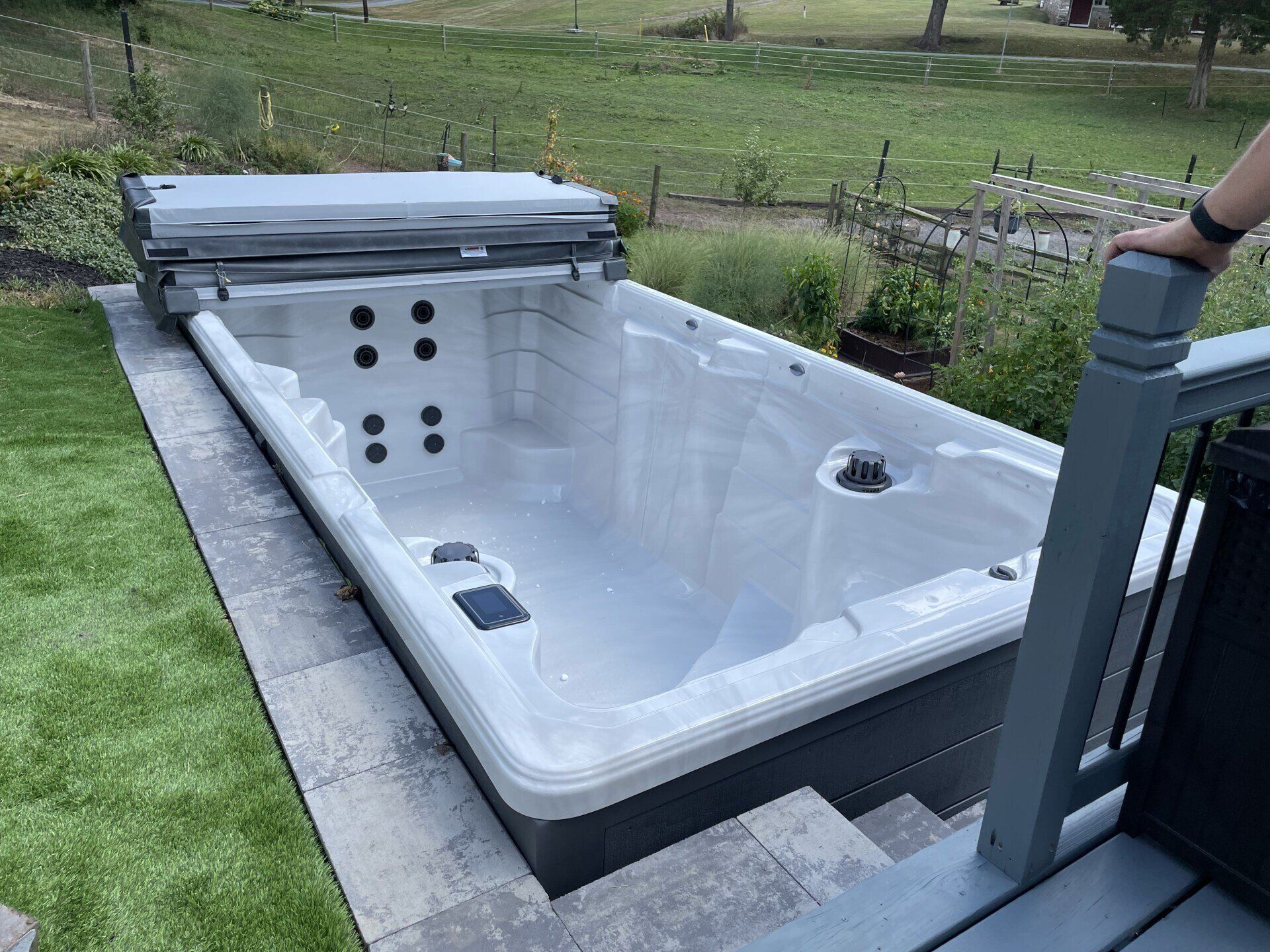 A rectangular swim spa with cover open, next to a deck and green yard.