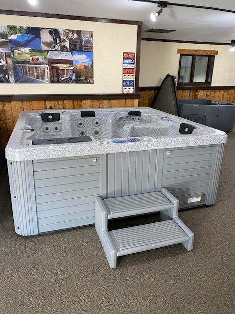 Gray hot tub with steps indoors, next to a wall with a picture.