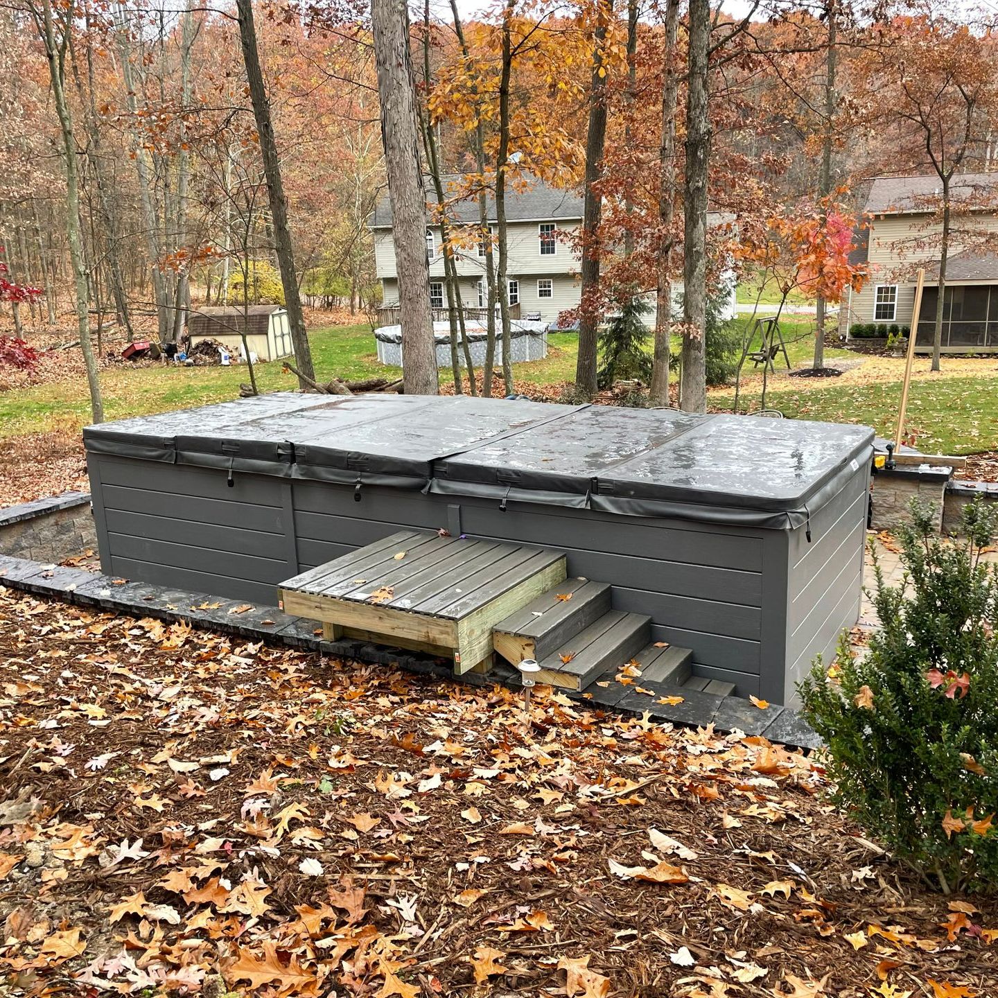 A large gray hot tub with steps outside, set among autumn foliage.