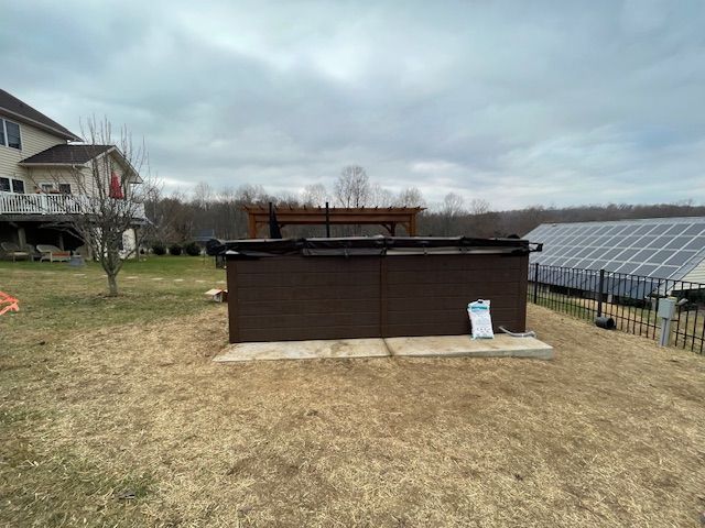 Hot tub on concrete pad in a backyard with cloudy sky and solar panels.