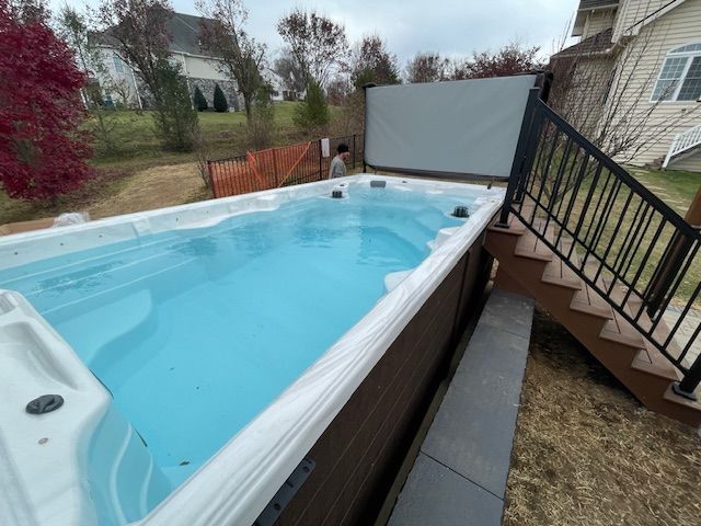 A rectangular swim spa with clear water, next to stairs and a fence, outdoors.