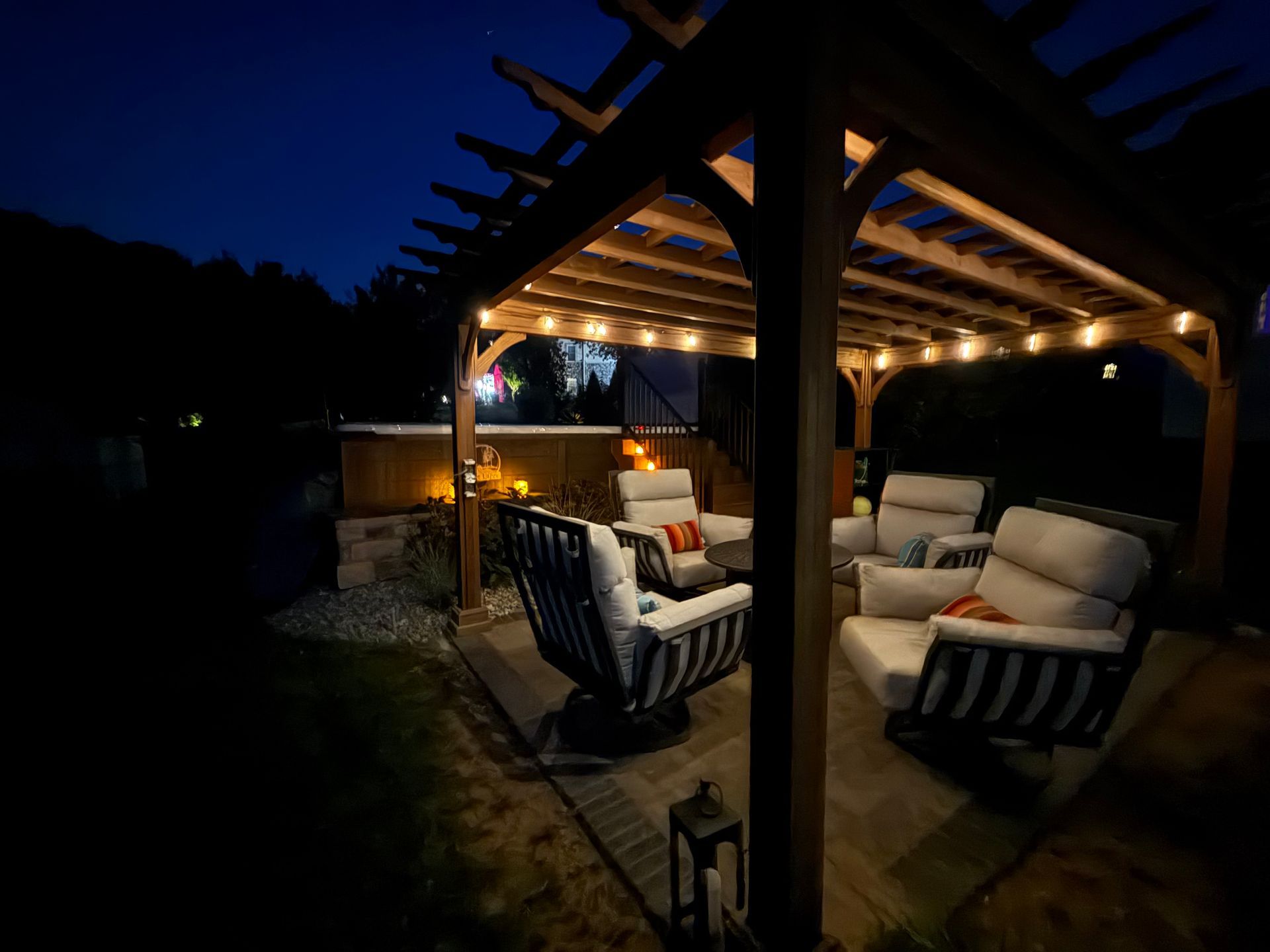 Outdoor seating area under a pergola at night, lit by string lights.