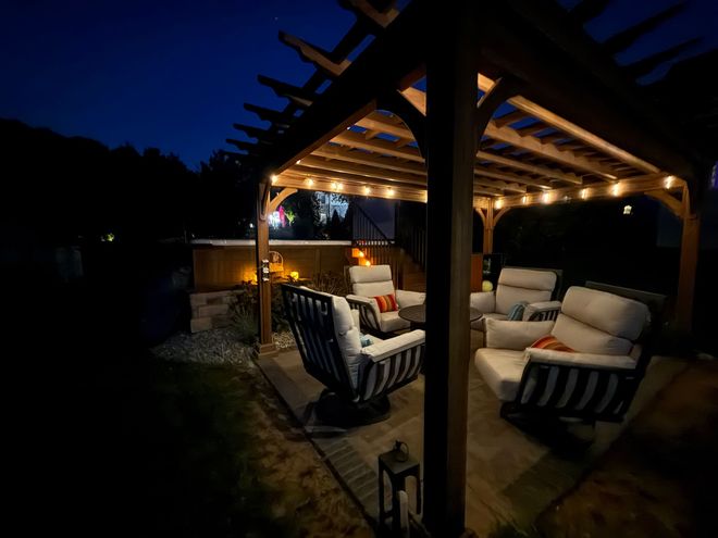 Outdoor seating area under a pergola at night, lit by string lights.