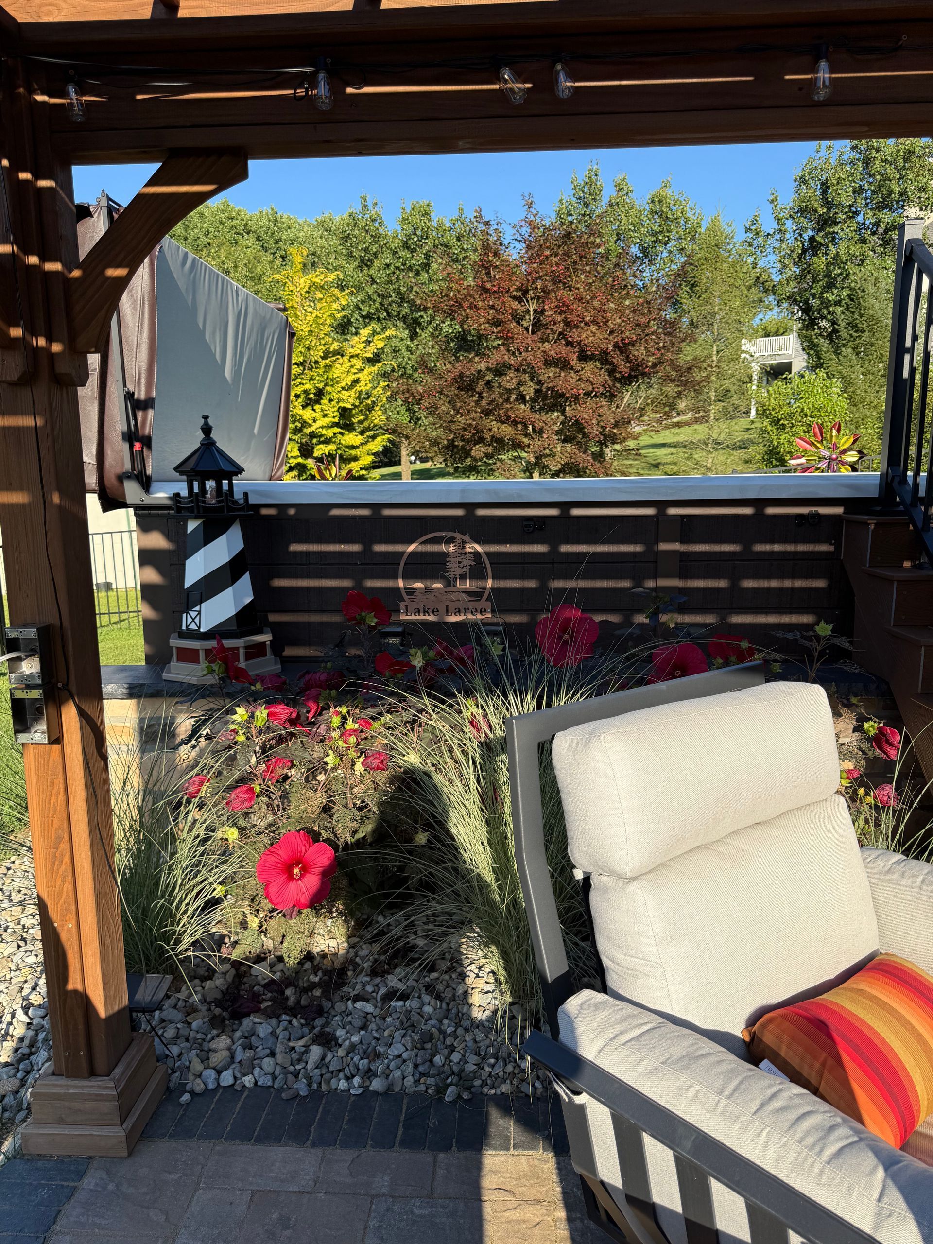 Patio scene with pergola, red flowers, and a white recliner chair in front of a garden.