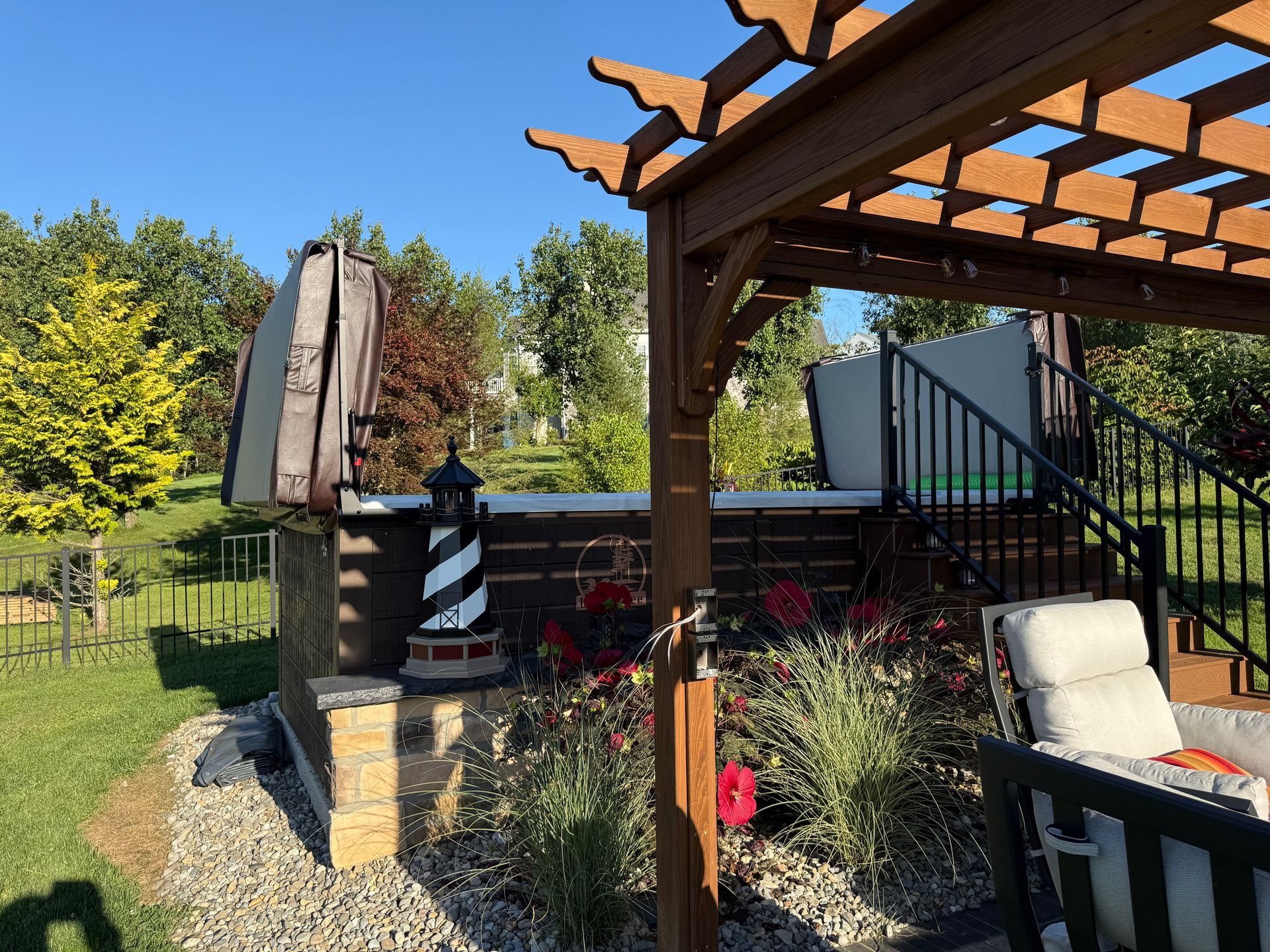 Hot tub with cover, pergola, lighthouse statue, and flowers in sunny backyard.