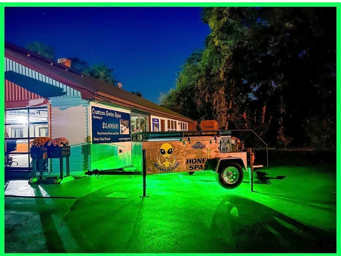 A brightly lit building at night with a trailer featuring alien artwork, reflecting green light onto the pavement.