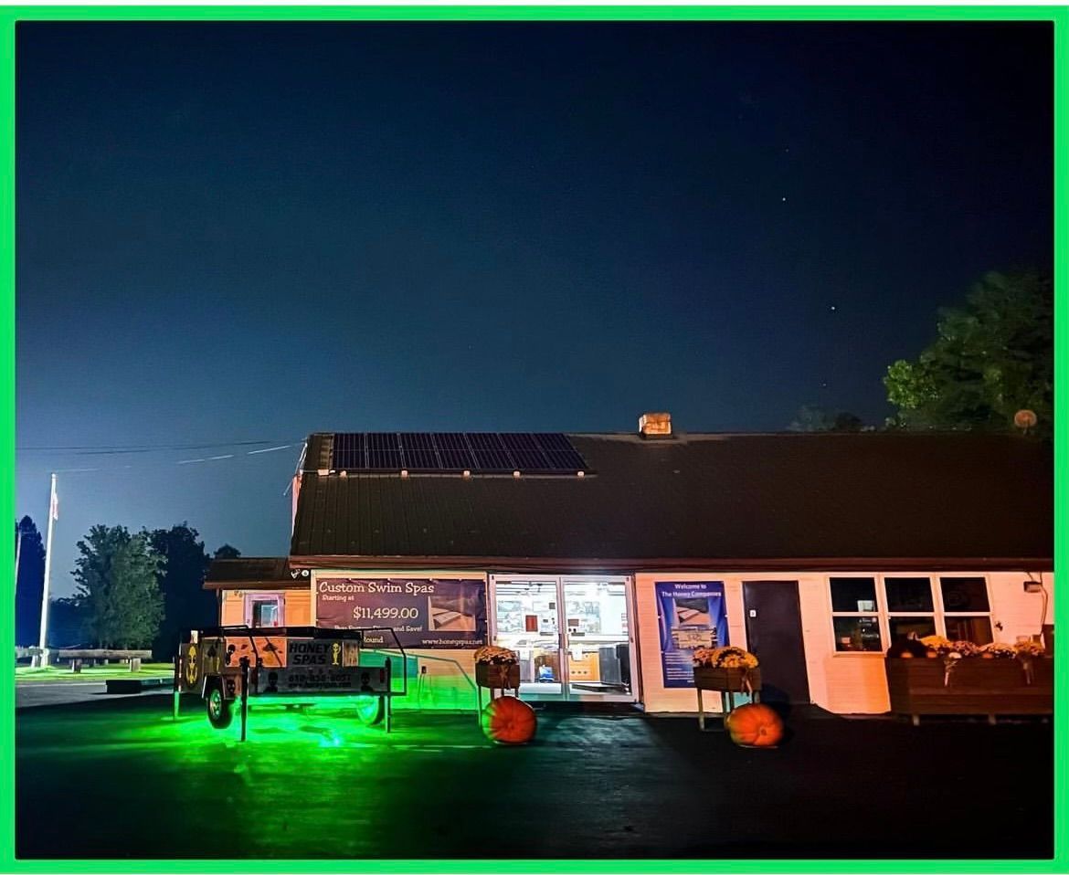 A brightly lit ice cream shop at night with green lights; pumpkins decorate the entrance. Solar panels on roof.