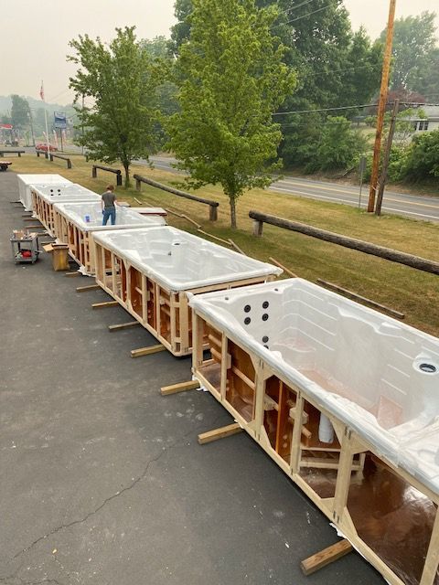 Hot tubs in wooden crates, lined up outside a building, with a person standing near the middle.