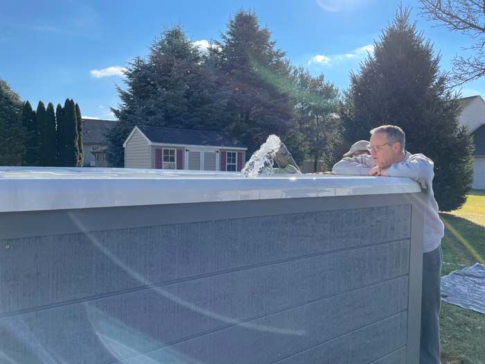 Man peering over the edge of a hot tub, outdoors on a sunny day.