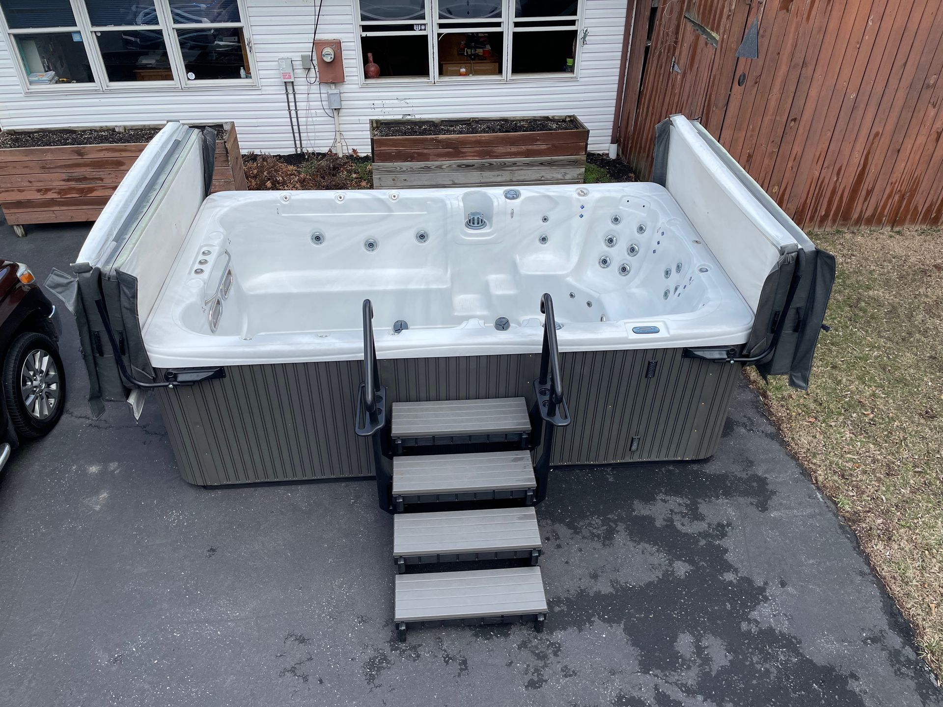 Hot tub with open cover and steps on a driveway.