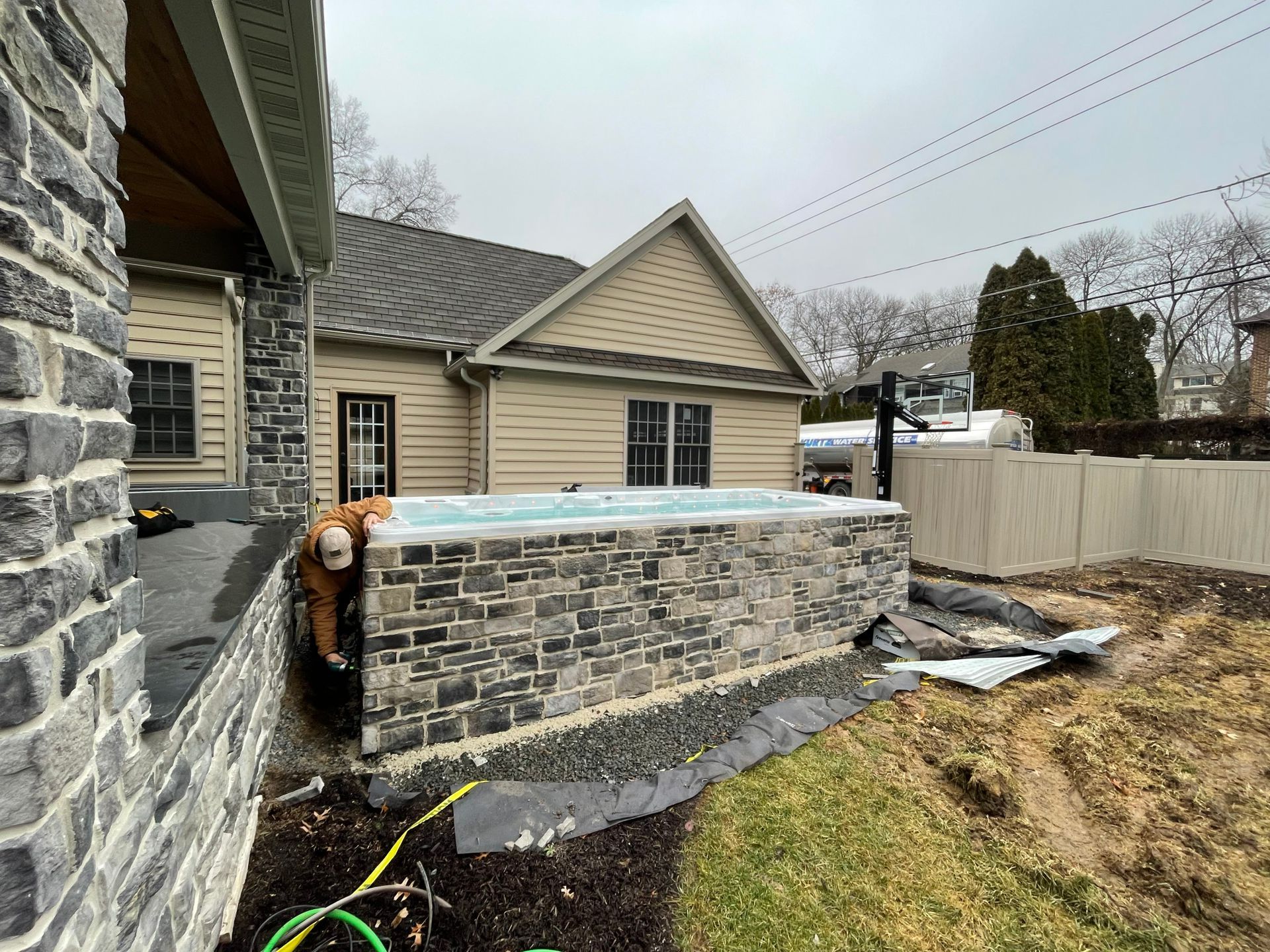 Hot tub encased in stone next to a house. A person works near the side.
