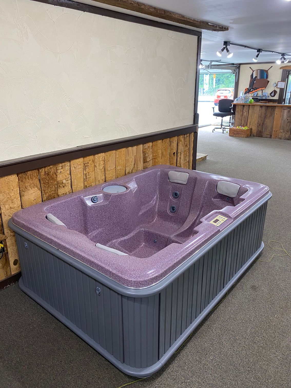 Hot tub with gray siding and a purple speckled interior, inside a shop.