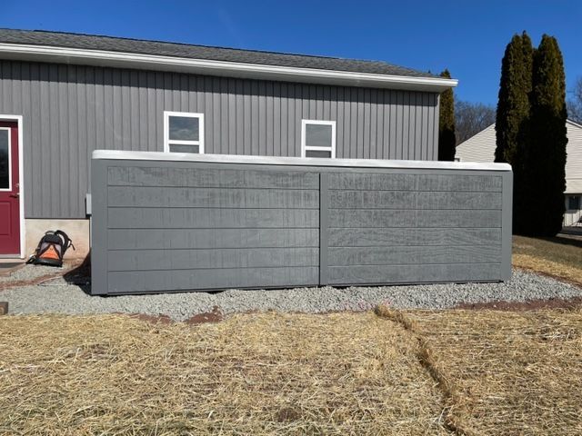 A large gray hot tub next to a building with gray siding, on a bed of rocks.